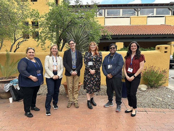 Members of the CI Compass team in attendance to the 2024 NSF RIW stand in a courtyard, with plants around them and a yellow stucco building behind them, smiling.