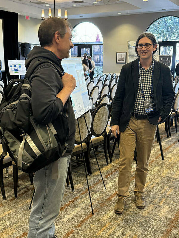 Two men are pictured at the 2024 NSF RIW poster session. One is looking away from the camera, while the other, Don Brower, is smiling mid-conversation.