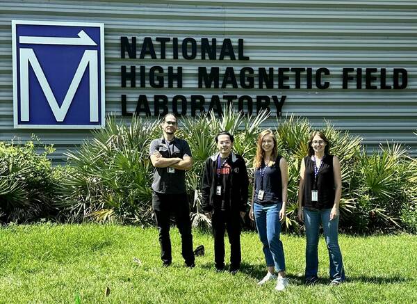 Four people stand outside in a lawn in front of a building with the sign for the National High Magnetic Field Laboratory.