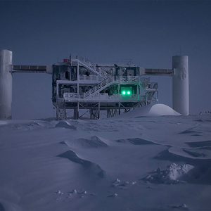 A photo shows the NSF IceCube Neutrino Observatory by moonlight, in a snowy landscape,