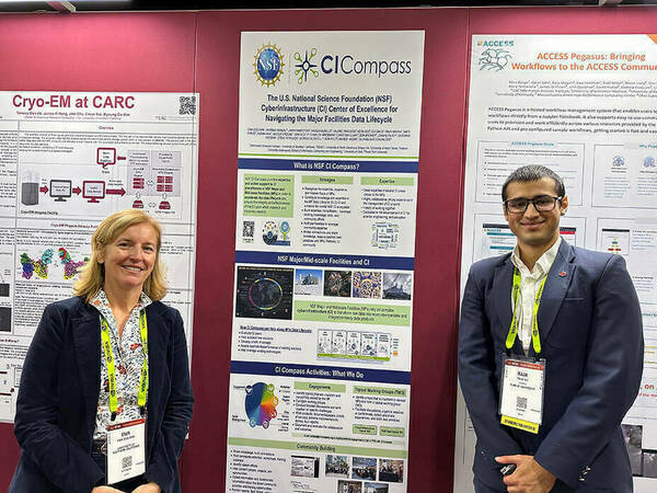 A photo of Ewa Deelman, a white woman with blonde hair who is smiling, with Raja Ali, a young Arab American man wearing glasses and smiling, stand before a CI Compass poster at SuperComputing 2024.