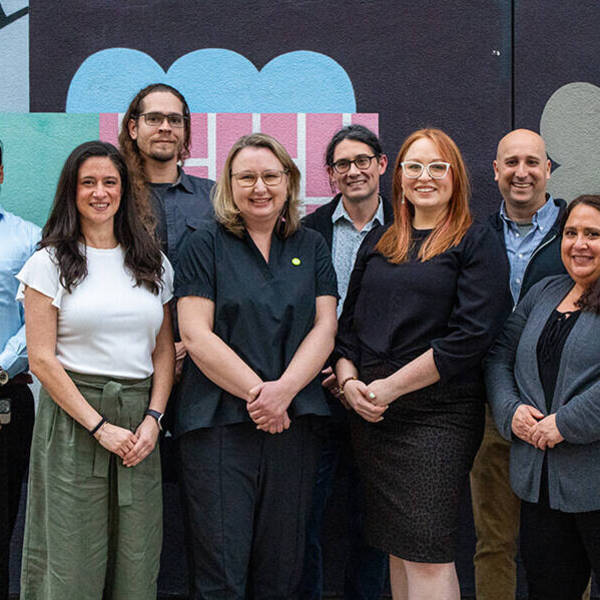 A group of FAIR TWG members stand together in front of a painted wall. This group includes 4 men and 4 women.