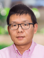 Headshot of a person with short dark hair, wearing glasses and a pink and white checkered shirt.