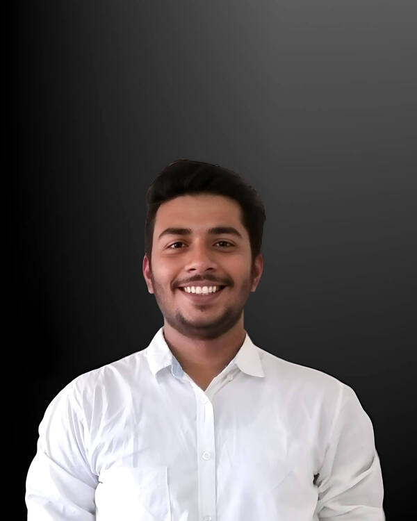 A smiling young man with dark hair and a short beard wears a white collared shirt, facing the viewer against a dark gradient background.